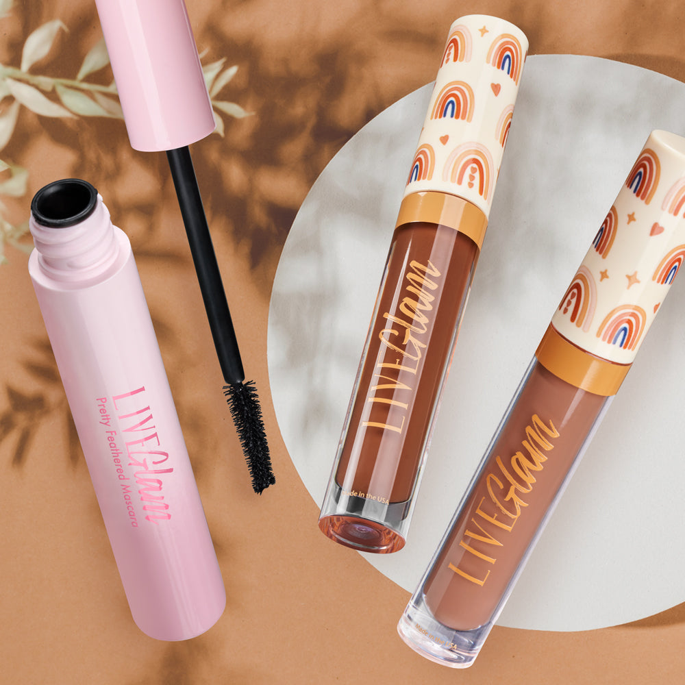 The three items from LiveGlam's Boho Dreamer collection, including a Peace + Love liquid lippie lip gloss, Pretty Feathered Mascara, and the Dreamer matte liquid lippie. The lippies feature a boho-design with hearts, stars and skintone colored rainbows.
The Mascara is opened, showing off the mascara applicator, the fine bristles and black mascara visibly coating the applicator bristles
