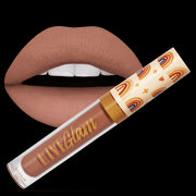 A bottle of the 'Dreamer' LiveGlam matte liquid lippie, with a cap featuring a boho-design with hearts, stars and skintone colored rainbows.
Behind the bottle is a pair of lips painted with the 'Dreamer' matte liquid lippie 