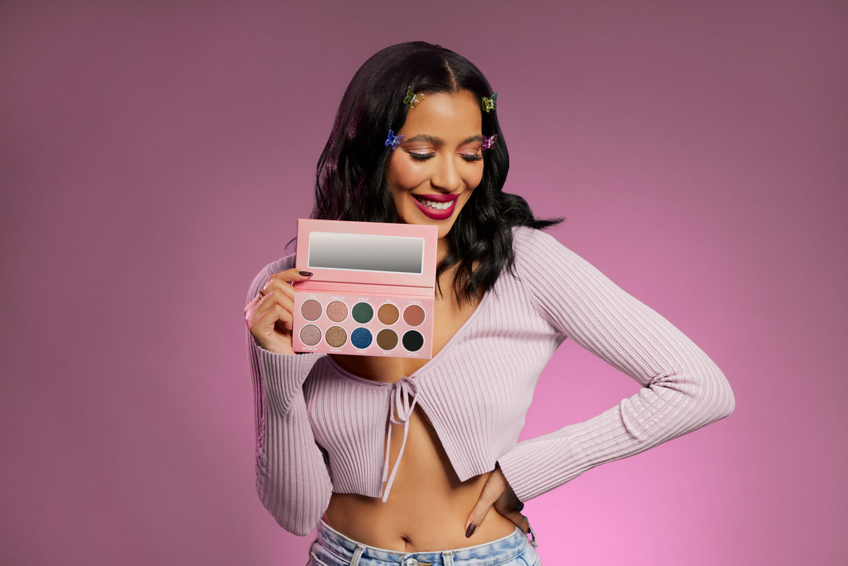 model with butterfly clips in her black hair holds up an eyeshadow palette: Understood the Assignment 10-pan palette. 