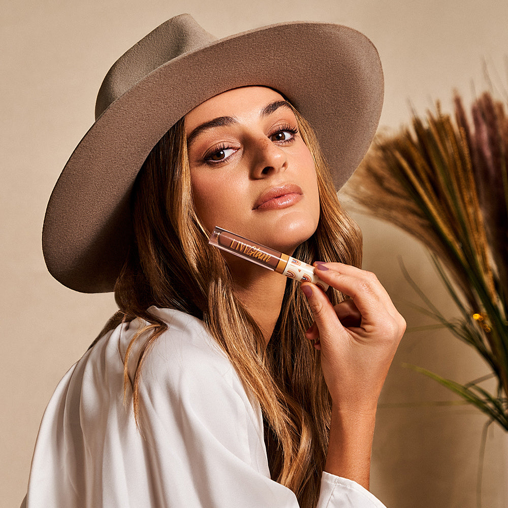 Model wearing a white blouse and a festival hat holding the Peace and Love lippie beneath her face