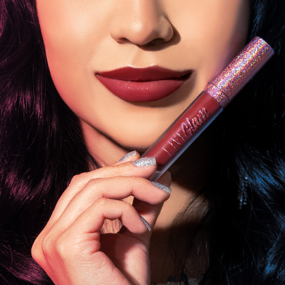 An extreme close-up of the model wearing with silver glitter nail polish as she shows off her bottle of Bell Bottom Babe gloss liquid lippie, which she holds beneath her face in her right hand. She already has the Disco Diva shade applied to her lips. The corners of her mouth are barely upturned in the coyest of faint smiles.