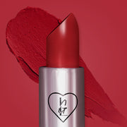 A close-up image of red Mami bullet lipstick in a true ruby red shade with a heart logo on the tube. Background shows a red backdrop as well as a thick red swatch from the bullet lippie
